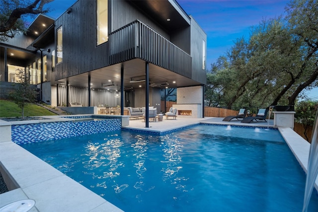 pool at dusk with an outdoor living space with a fireplace, a patio area, ceiling fan, and an in ground hot tub