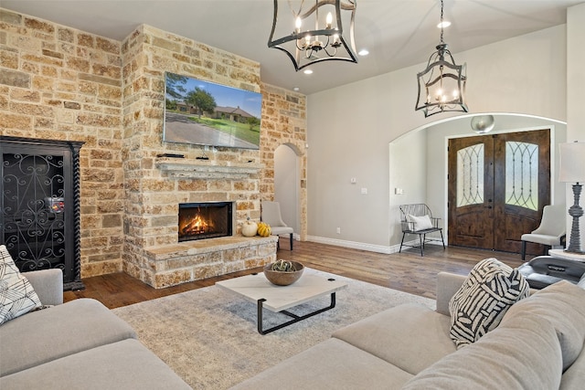 living room featuring hardwood / wood-style flooring, a stone fireplace, french doors, and a notable chandelier