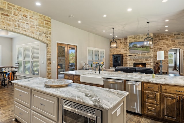 kitchen featuring brick wall, a fireplace, stainless steel appliances, a center island with sink, and sink