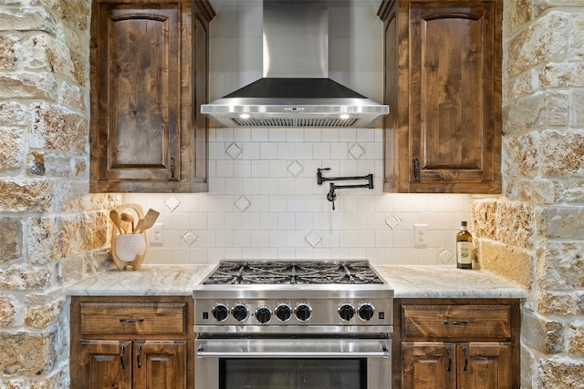 kitchen featuring backsplash, wall chimney exhaust hood, light stone countertops, and stainless steel range