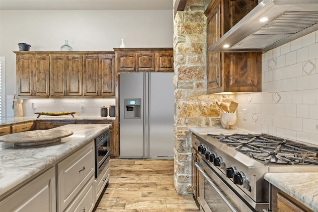 kitchen with wall chimney exhaust hood, light hardwood / wood-style floors, appliances with stainless steel finishes, and tasteful backsplash