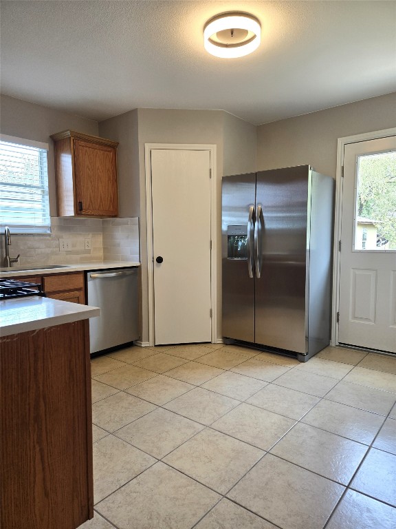 kitchen with appliances with stainless steel finishes, backsplash, light tile patterned floors, and a wealth of natural light