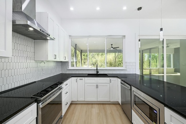 kitchen with appliances with stainless steel finishes, sink, wall chimney range hood, decorative light fixtures, and white cabinets