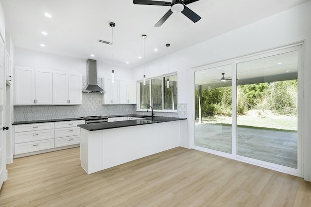 kitchen featuring kitchen peninsula, light wood-type flooring, hanging light fixtures, and wall chimney range hood