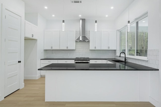 kitchen with decorative light fixtures, wall chimney range hood, kitchen peninsula, and stainless steel range with gas stovetop