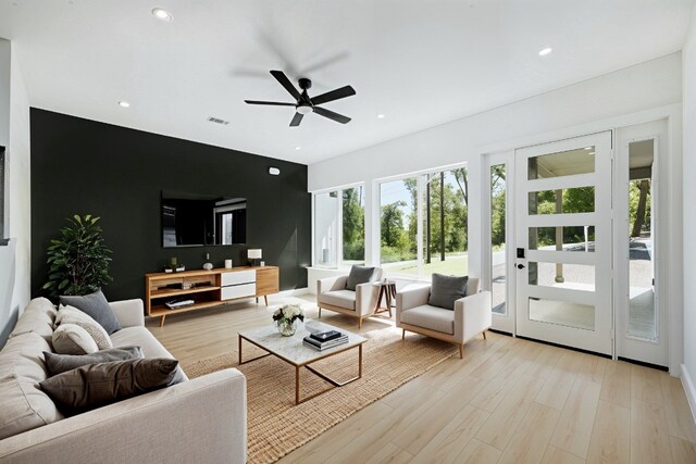 living room featuring a ceiling fan, visible vents, recessed lighting, light wood-style floors, and an accent wall