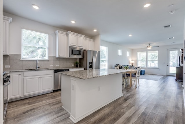 kitchen with light wood-type flooring, sink, white cabinetry, a kitchen island, and appliances with stainless steel finishes