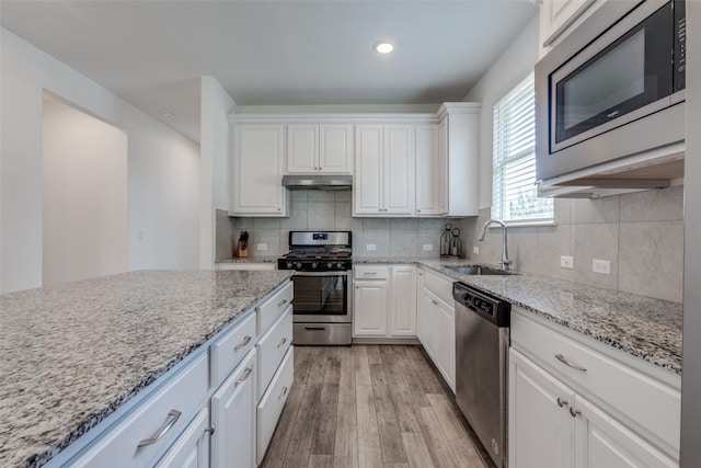 kitchen with tasteful backsplash, light hardwood / wood-style flooring, white cabinetry, stainless steel appliances, and light stone countertops