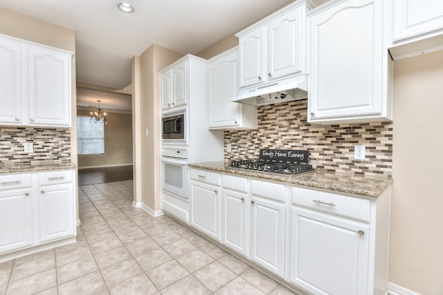 kitchen with stainless steel appliances, white cabinets, light stone counters, and a chandelier