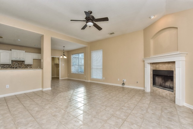 unfurnished living room featuring ceiling fan with notable chandelier, a tile fireplace, light tile patterned flooring, and sink