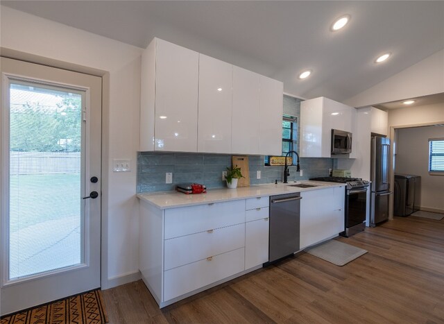 kitchen with appliances with stainless steel finishes, a healthy amount of sunlight, vaulted ceiling, and white cabinets