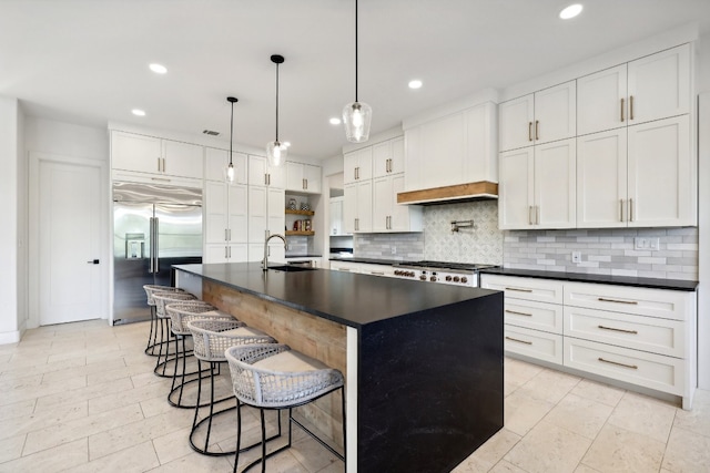 kitchen featuring pendant lighting, sink, an island with sink, white cabinets, and built in refrigerator