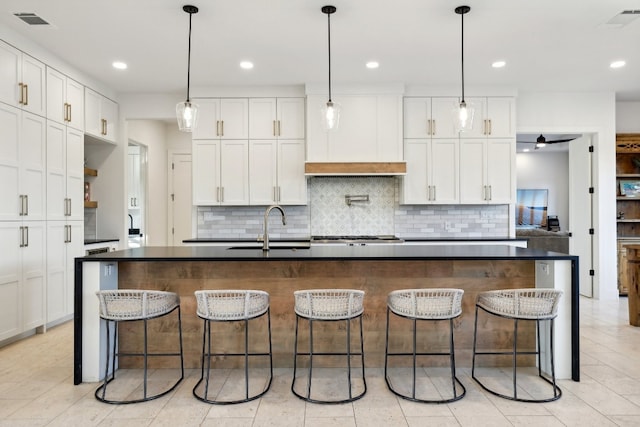 kitchen with hanging light fixtures, tasteful backsplash, a kitchen island with sink, white cabinetry, and a breakfast bar area