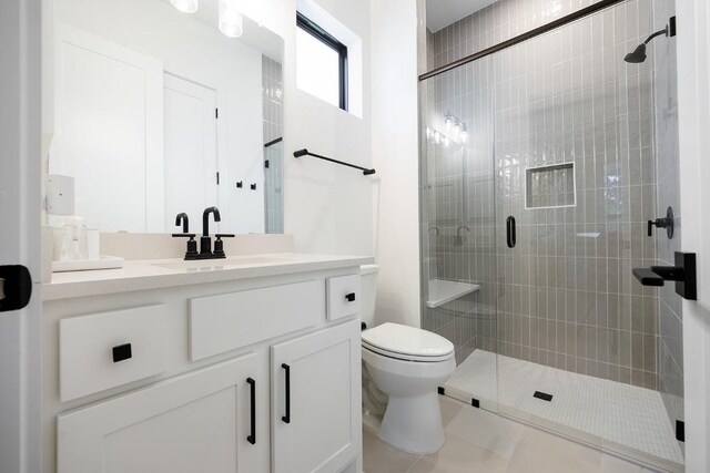 bathroom featuring tile patterned flooring, vanity, toilet, and a shower with door