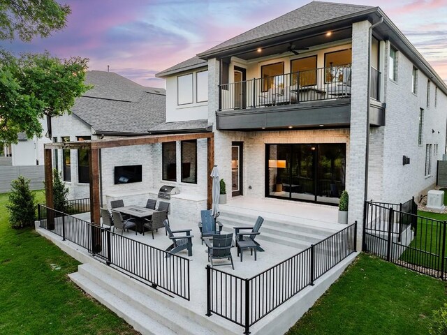 back house at dusk featuring a yard, ceiling fan, a balcony, and a patio