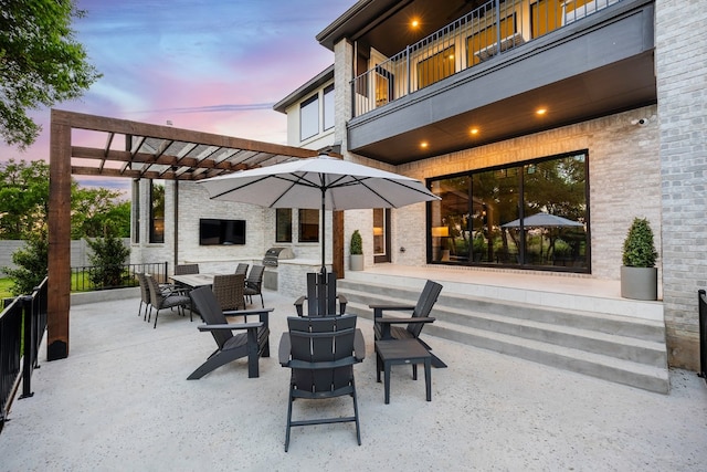 patio terrace at dusk with a pergola, a balcony, and exterior kitchen