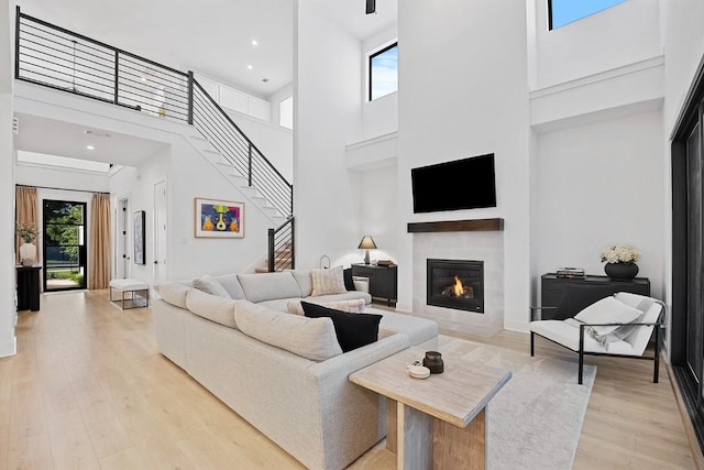 living room featuring a fireplace with flush hearth, stairs, a high ceiling, light wood-style floors, and recessed lighting