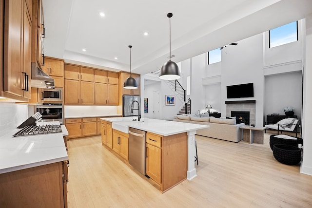 kitchen featuring light stone countertops, stainless steel appliances, pendant lighting, a center island with sink, and light wood-type flooring