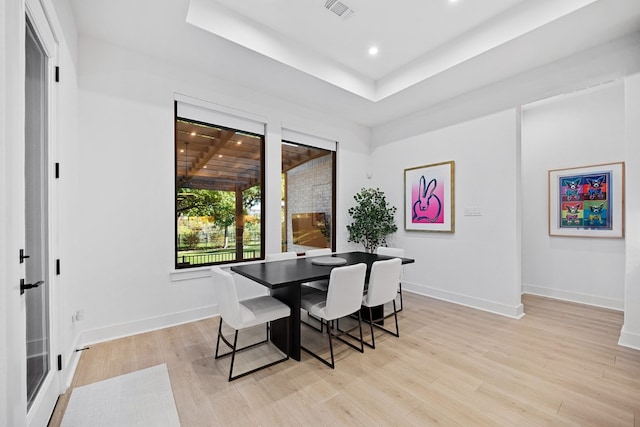 dining space with light hardwood / wood-style floors and a tray ceiling