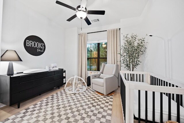 bedroom with ceiling fan, a crib, and light hardwood / wood-style flooring