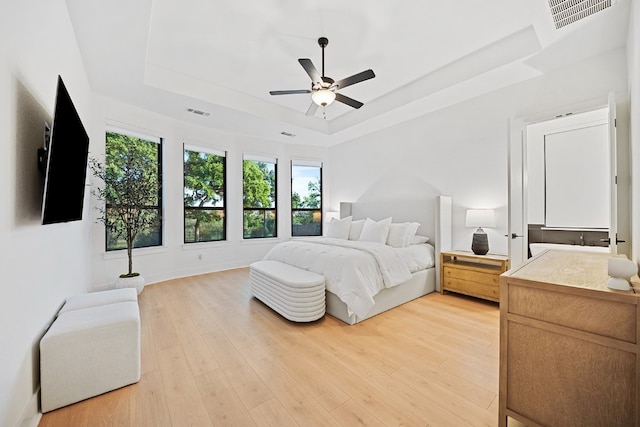 bedroom featuring a raised ceiling, ceiling fan, and light wood-type flooring