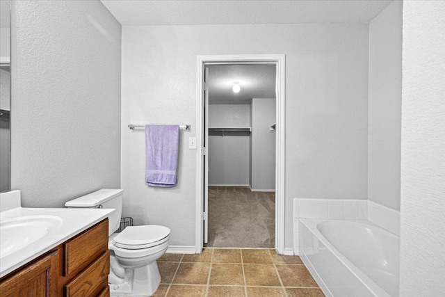 bathroom with a garden tub, a spacious closet, toilet, vanity, and tile patterned floors