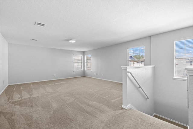 spare room featuring light carpet, baseboards, visible vents, and a textured ceiling