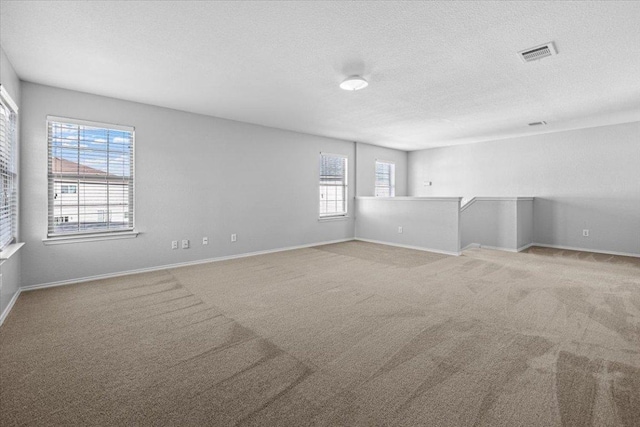 carpeted empty room with baseboards, visible vents, and a textured ceiling