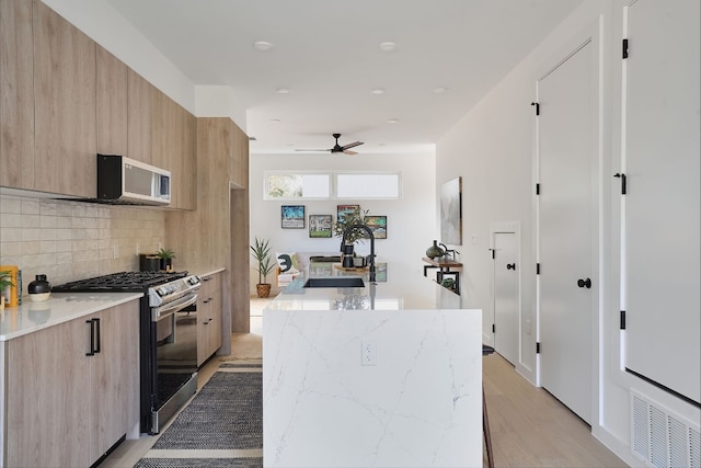 kitchen featuring sink, an island with sink, light hardwood / wood-style floors, light stone counters, and stainless steel appliances