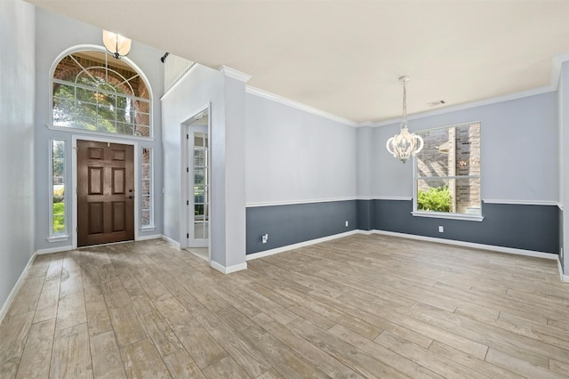 entrance foyer featuring light wood-type flooring, ornamental molding, and a notable chandelier