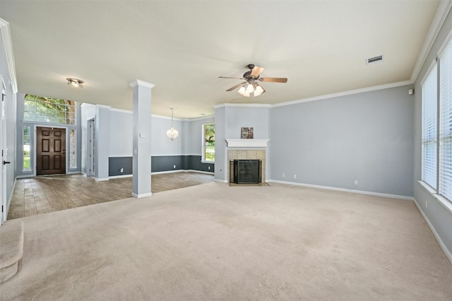 unfurnished living room with a tile fireplace, ornate columns, crown molding, ceiling fan, and light carpet