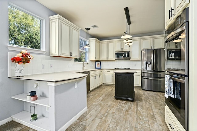 kitchen featuring appliances with stainless steel finishes, cream cabinets, pendant lighting, and tasteful backsplash