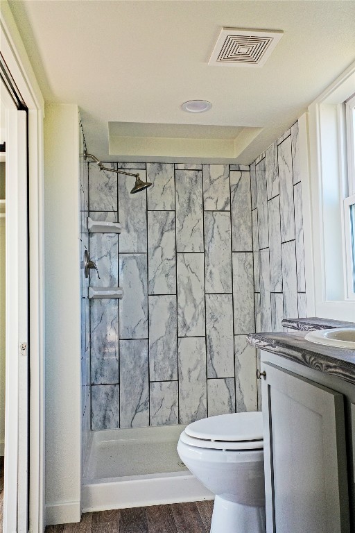 bathroom with a tile shower, hardwood / wood-style flooring, vanity, and toilet