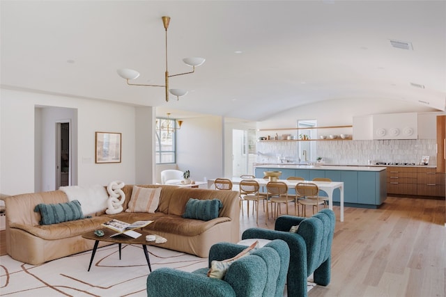 living room featuring vaulted ceiling, light hardwood / wood-style flooring, and a notable chandelier