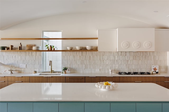 kitchen featuring lofted ceiling, stainless steel gas cooktop, sink, and tasteful backsplash