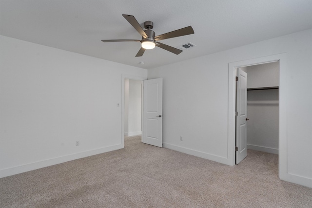 unfurnished bedroom with a walk in closet, a closet, light colored carpet, and ceiling fan