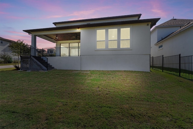 back house at dusk featuring ceiling fan and a lawn