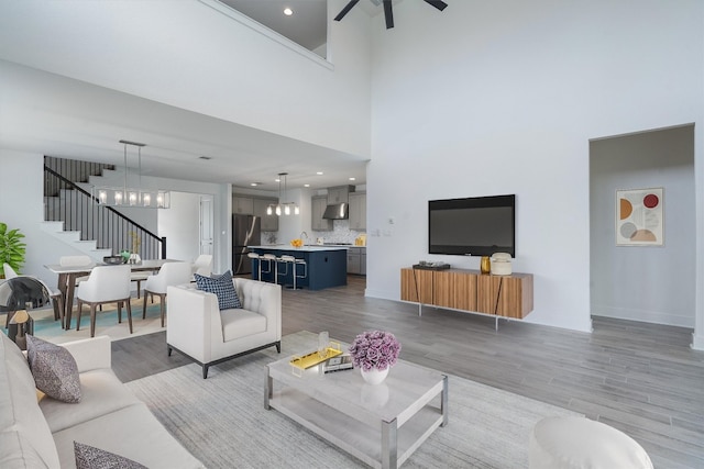 living room with ceiling fan with notable chandelier, sink, a high ceiling, and light hardwood / wood-style flooring