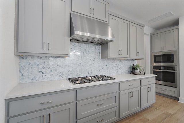 kitchen featuring gray cabinetry, decorative backsplash, light hardwood / wood-style floors, and appliances with stainless steel finishes