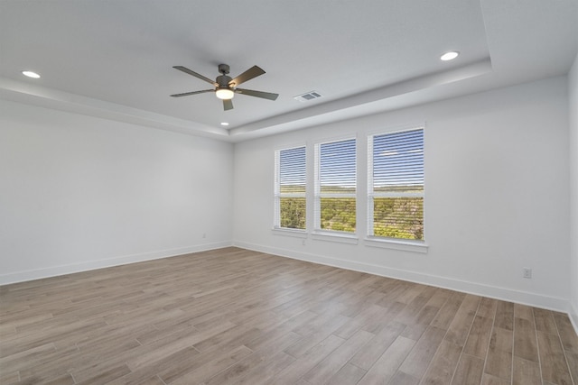 unfurnished room featuring ceiling fan, light hardwood / wood-style floors, and a tray ceiling