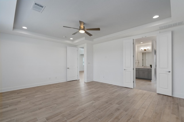 unfurnished bedroom featuring a tray ceiling, ensuite bath, and ceiling fan