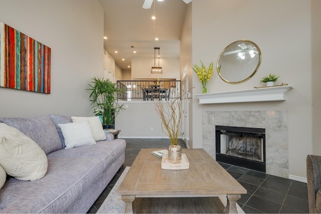 living room featuring ceiling fan, a high ceiling, and a tile fireplace