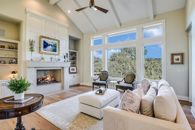 living area featuring plenty of natural light, a fireplace with flush hearth, light wood-style floors, and beamed ceiling