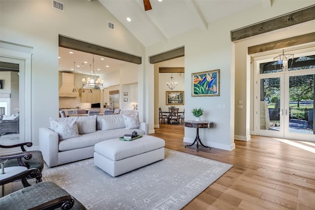 living area featuring high vaulted ceiling, light wood-style flooring, visible vents, and an inviting chandelier