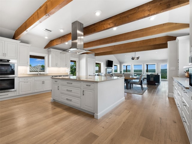 kitchen with white cabinets, island exhaust hood, a center island, and a wealth of natural light