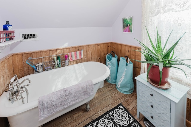 bathroom featuring vaulted ceiling, a tub to relax in, wood walls, and hardwood / wood-style floors