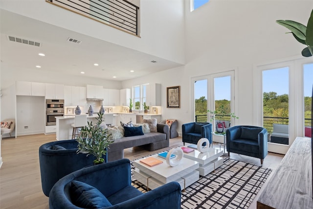 living room with french doors, light wood-type flooring, and a towering ceiling