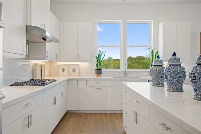 kitchen with stainless steel gas stovetop, light hardwood / wood-style floors, white cabinetry, and tasteful backsplash