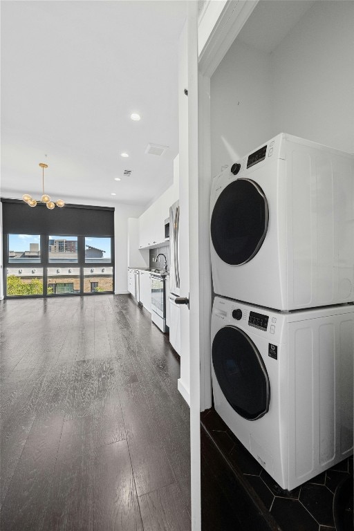 laundry room with a chandelier, stacked washer / dryer, and dark wood-type flooring