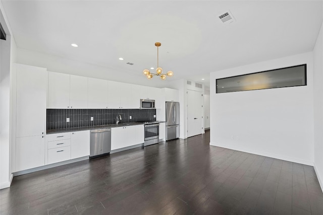 kitchen with appliances with stainless steel finishes, hanging light fixtures, dark wood-type flooring, and white cabinetry